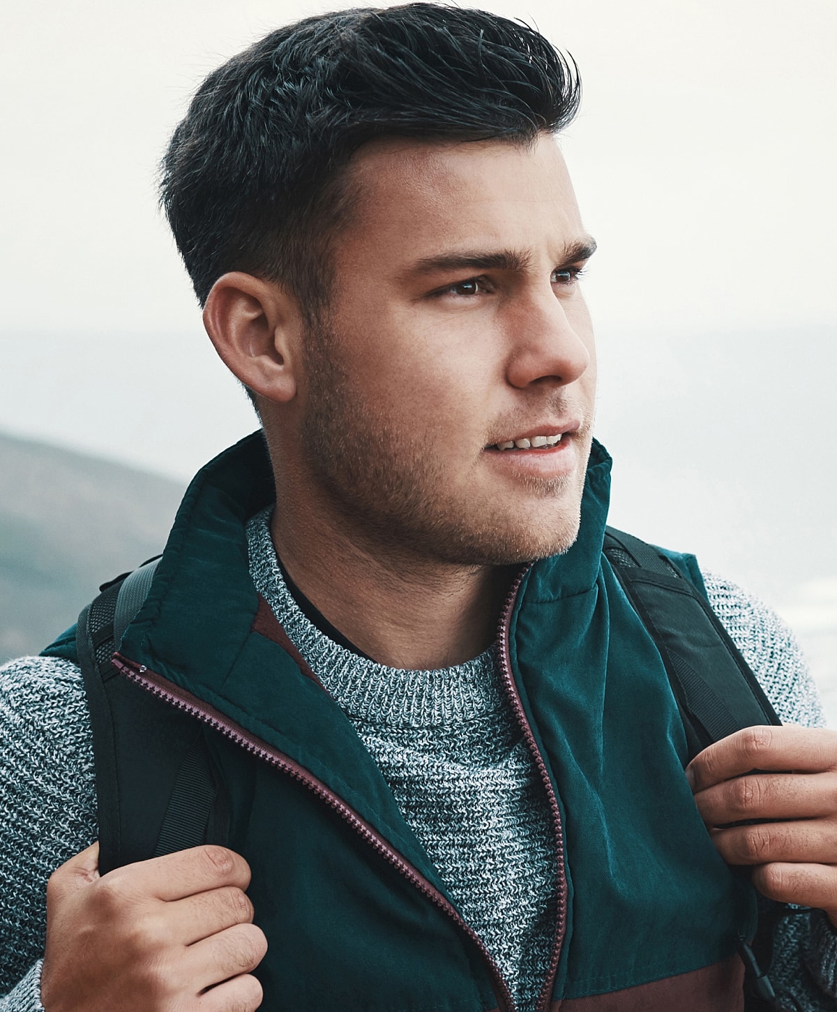Young man outdoors with backpack and cozy sweater.