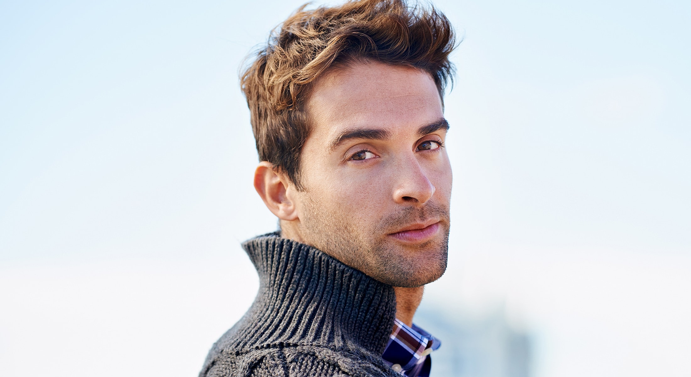 Man in a cozy sweater outdoors, looking back.