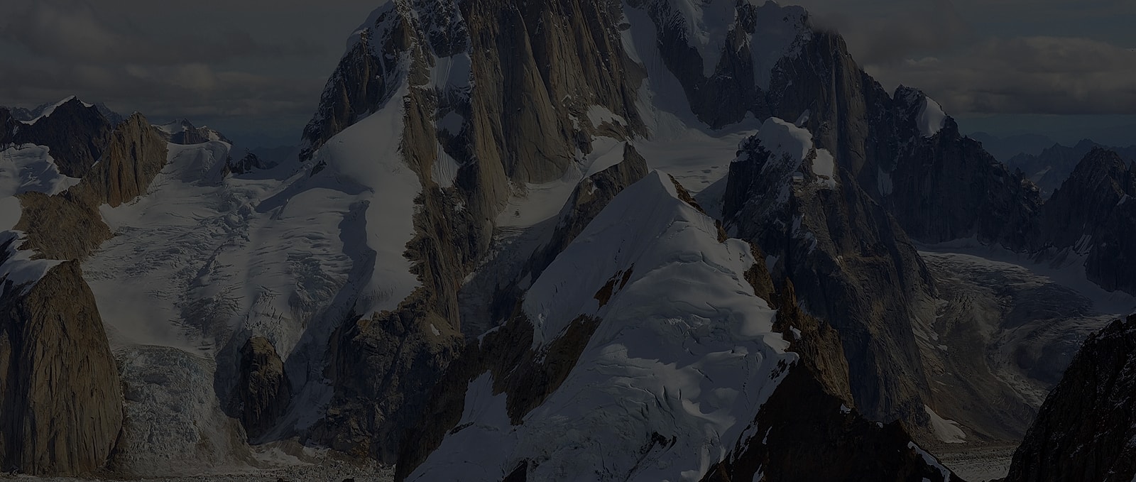 Snow-covered mountains with glaciers under a cloudy sky.