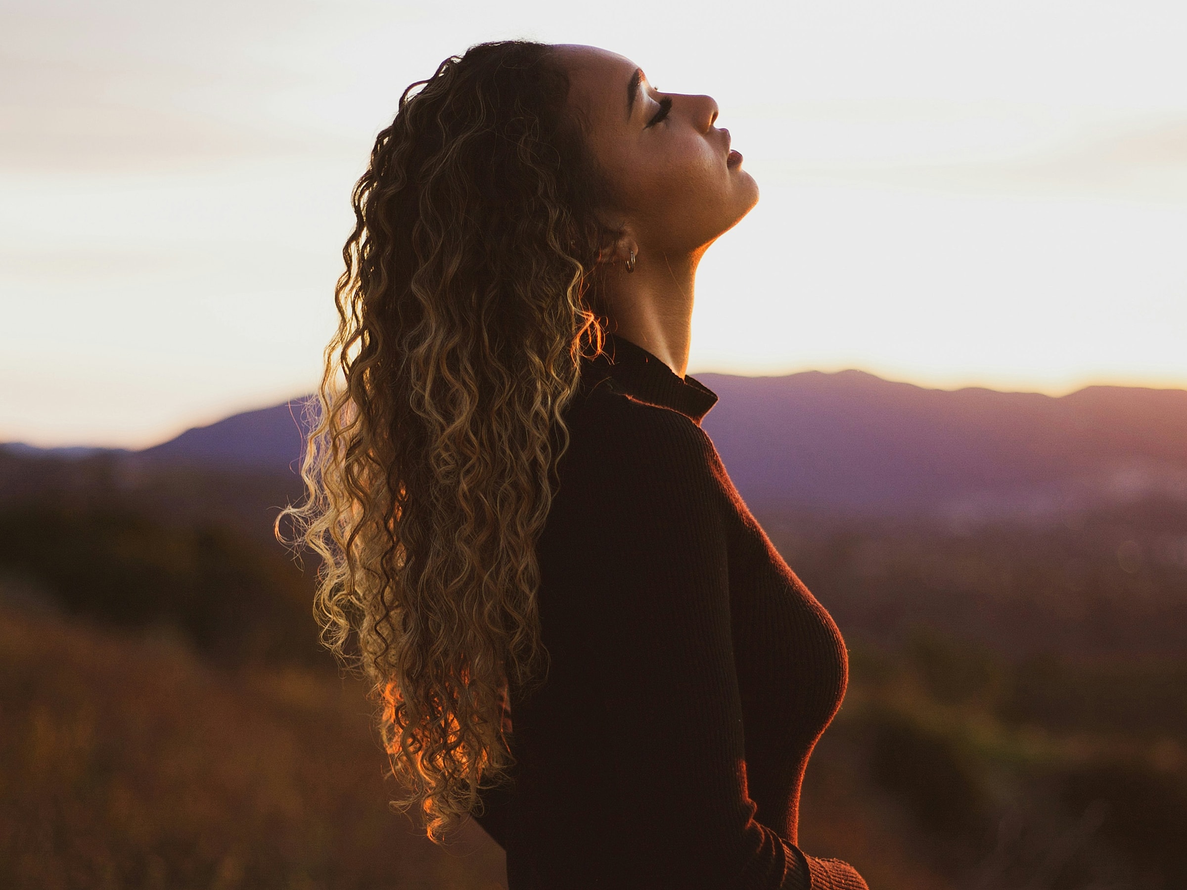 Woman looking upwards against sunset background.